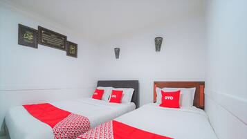 A hotel room with two beds, each with a red and white patterned bedspread and a red pillow with the hotel logo. There are three framed plaques on the wall, and a small decorative item above the beds.