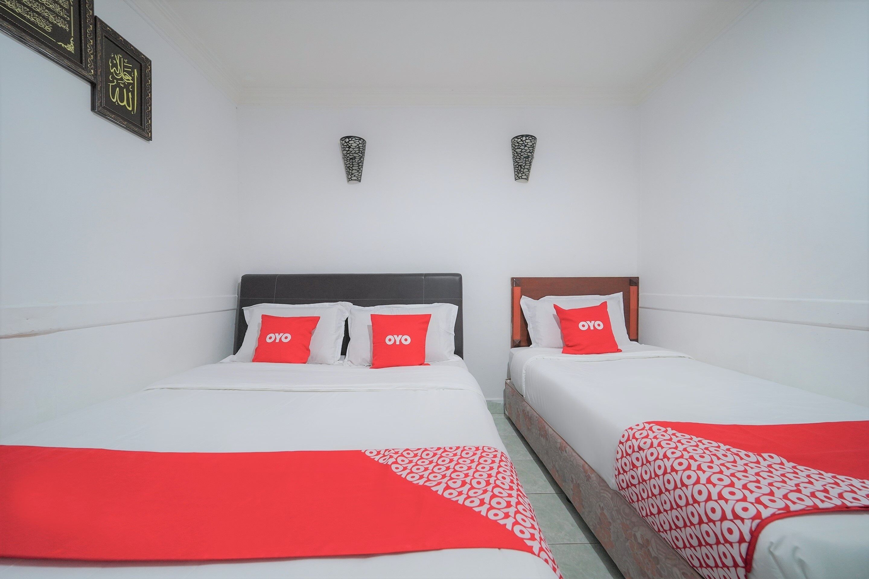 A hotel room with two beds, each with white bedding and red accents, including pillows and a blanket.