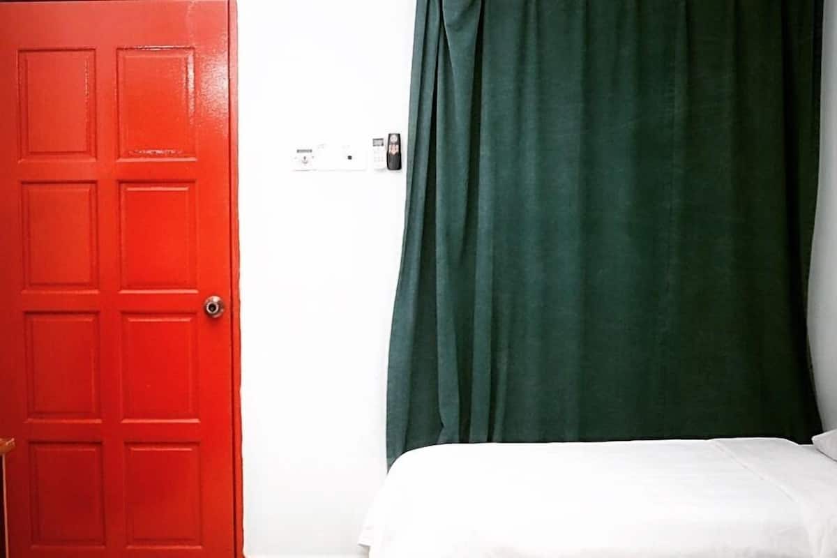 Una habitación con puerta roja, cama con ropa de cama blanca y cortina verde.