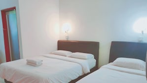 Une chambre d’hôtel avec deux lits, chacun doté de draps et d’oreillers blancs, d’une tête de lit en bois et d’un luminaire fixé au mur.