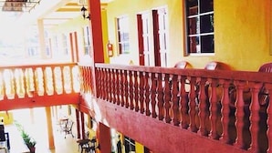 Un hôtel à plusieurs étages doté d’un balcon, de rampes en bois et d’une façade jaune.