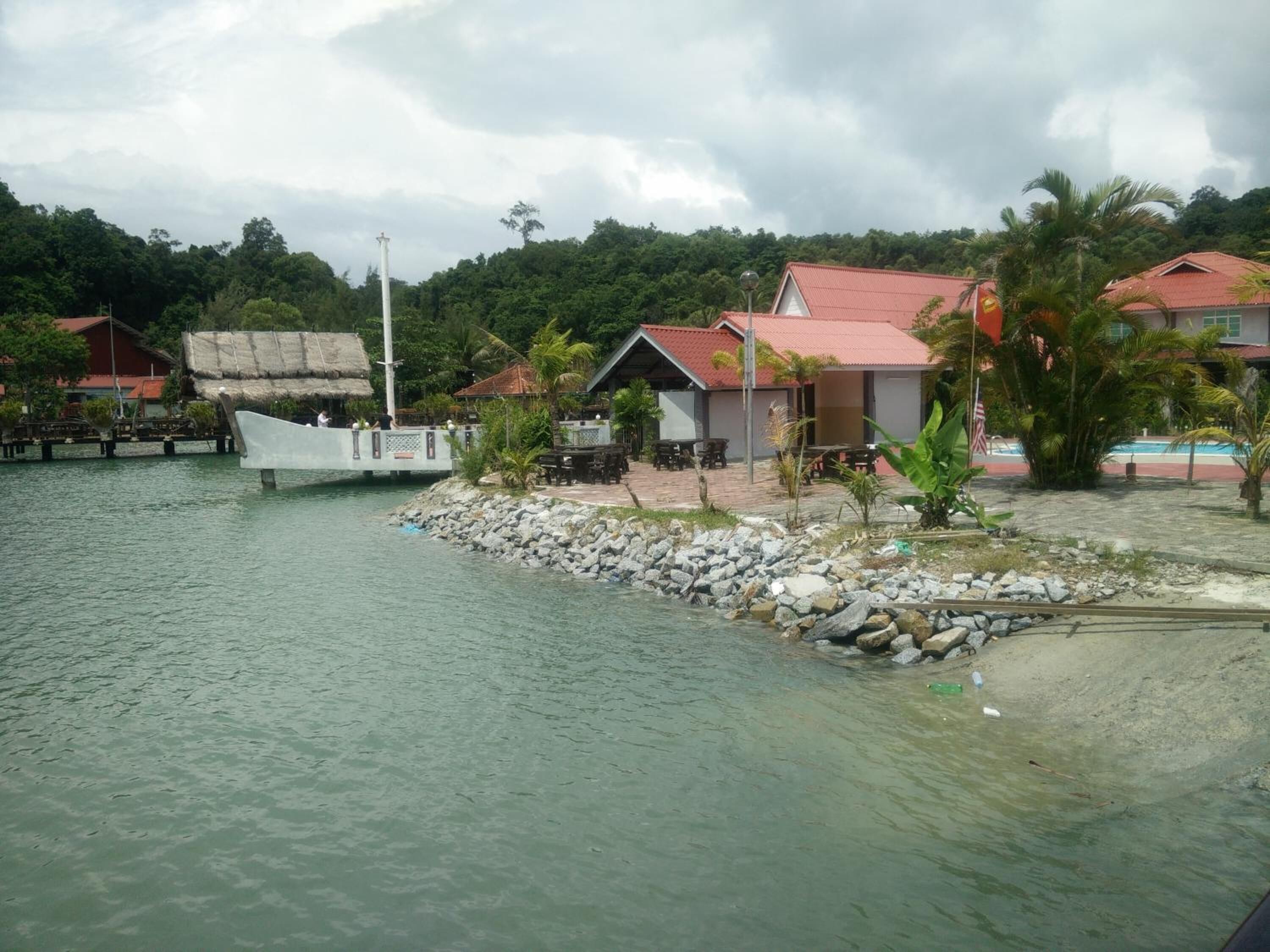 A coastal property with a dock, a small building with a red roof, and a thatched-roof structure.