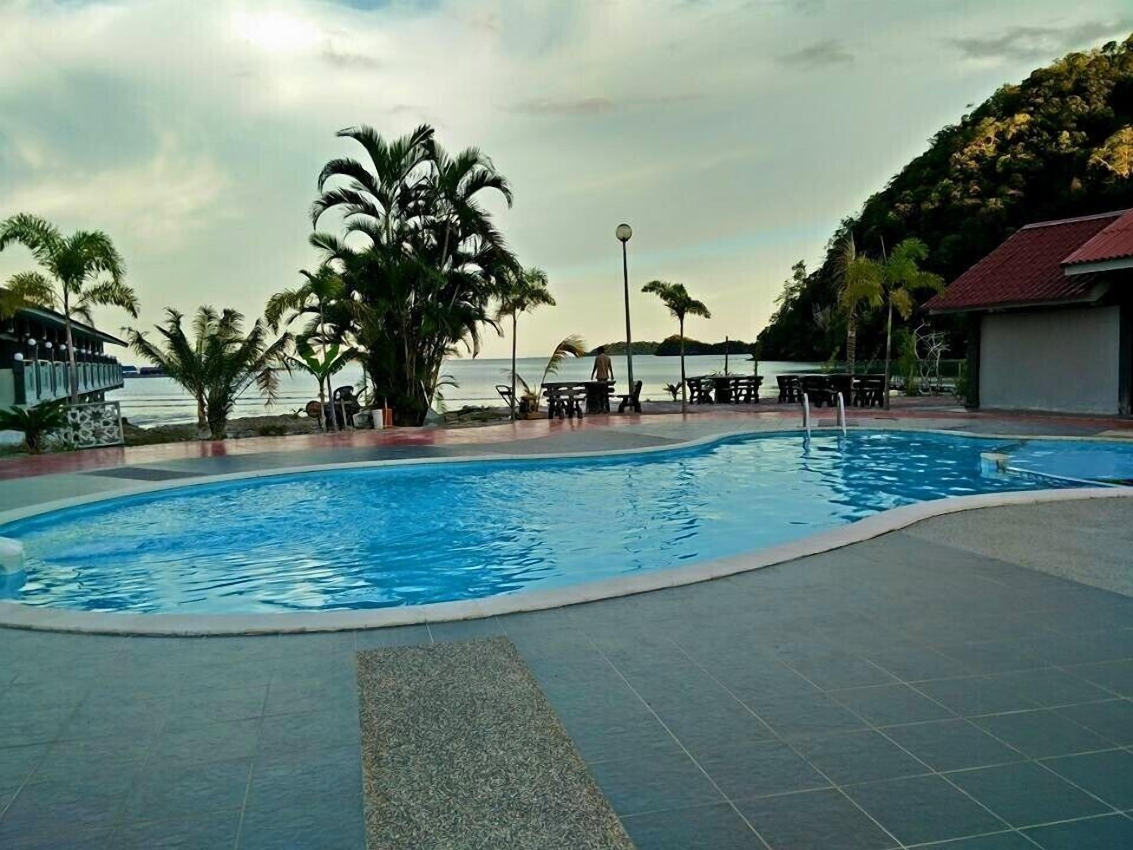 A swimming pool with a view of the sea, surrounded by palm trees and outdoor seating.