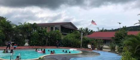 A swimming pool area with multiple pools, surrounded by greenery and buildings.