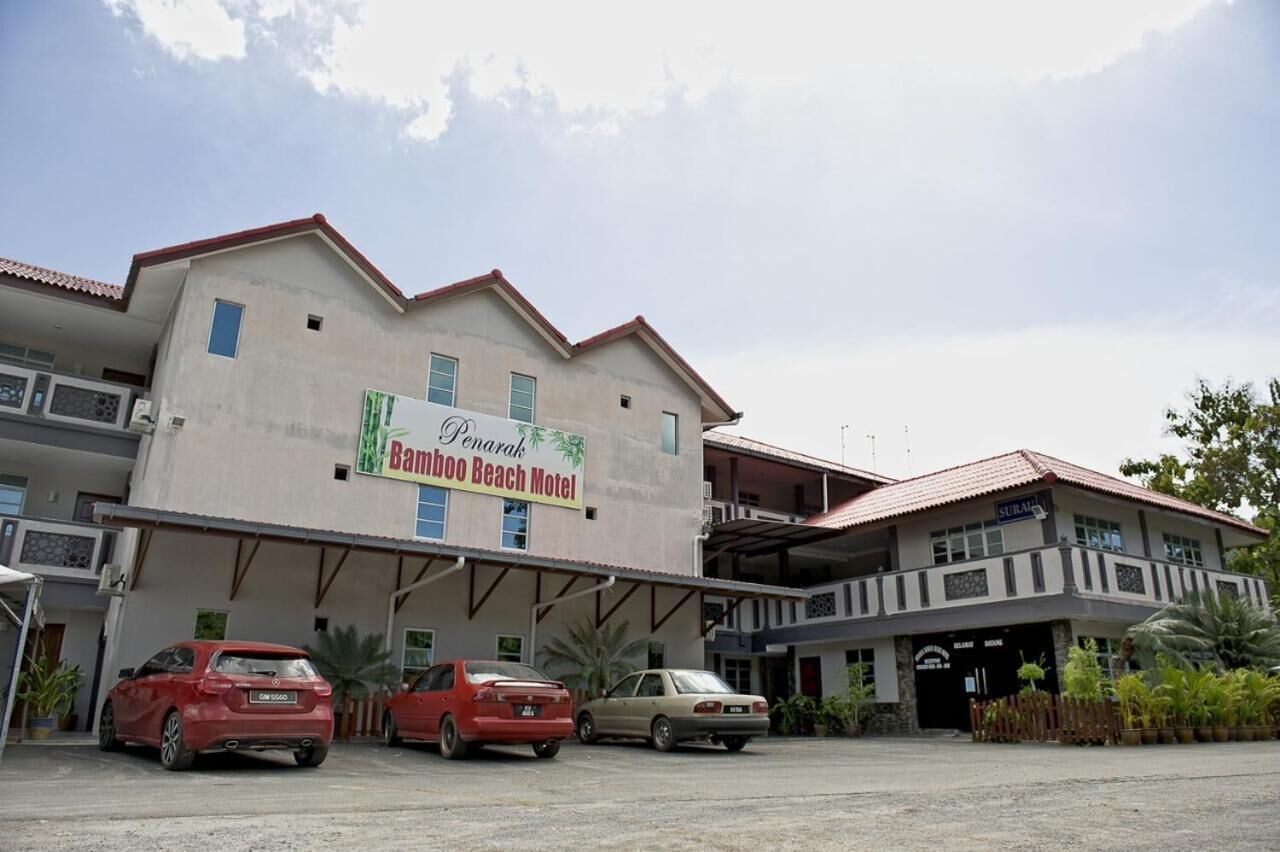 Een gebouw met een bord waarop 'Bamboo Beach Motel' staat. Drie auto's staan ervoor geparkeerd.