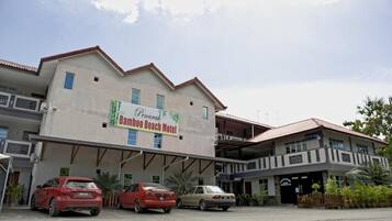 Een gebouw met een bord waarop 'Bamboo Beach Motel' staat. Drie auto's staan ervoor geparkeerd.