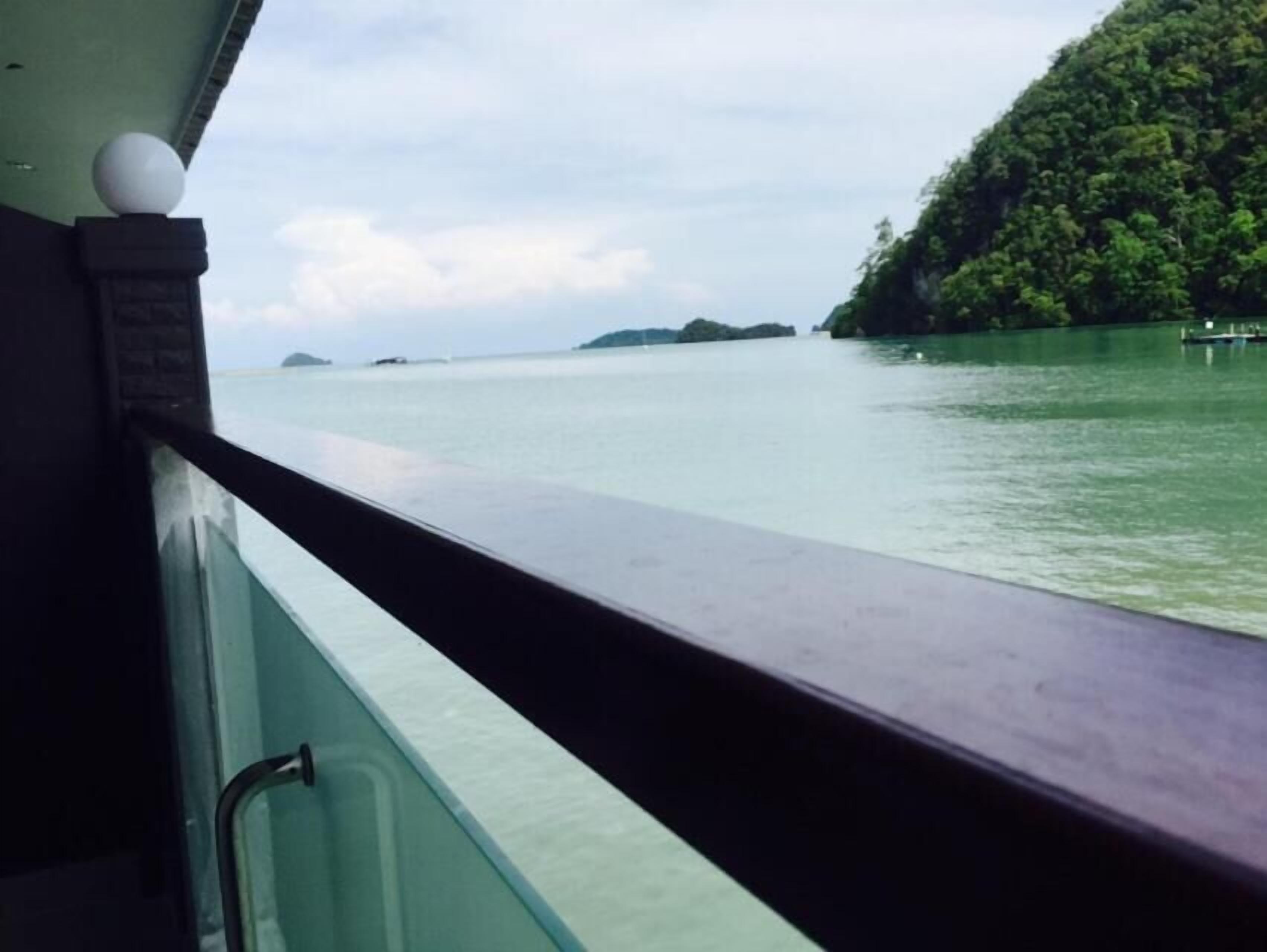 Vista desde un bote con barandilla, agua y una isla boscosa en la distancia.