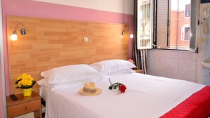 A neatly made bed with white linens, a wooden headboard, and a red accent at the foot. A yellow flower vase and a hat are on the nightstand beside the bed. - Hotel New Milan (Milan)