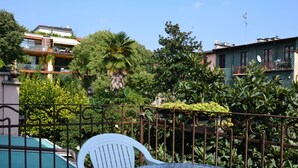 A balcony with a glass table and a white chair, surrounded by lush greenery and a pool. - Hotel New Milan (Milan)