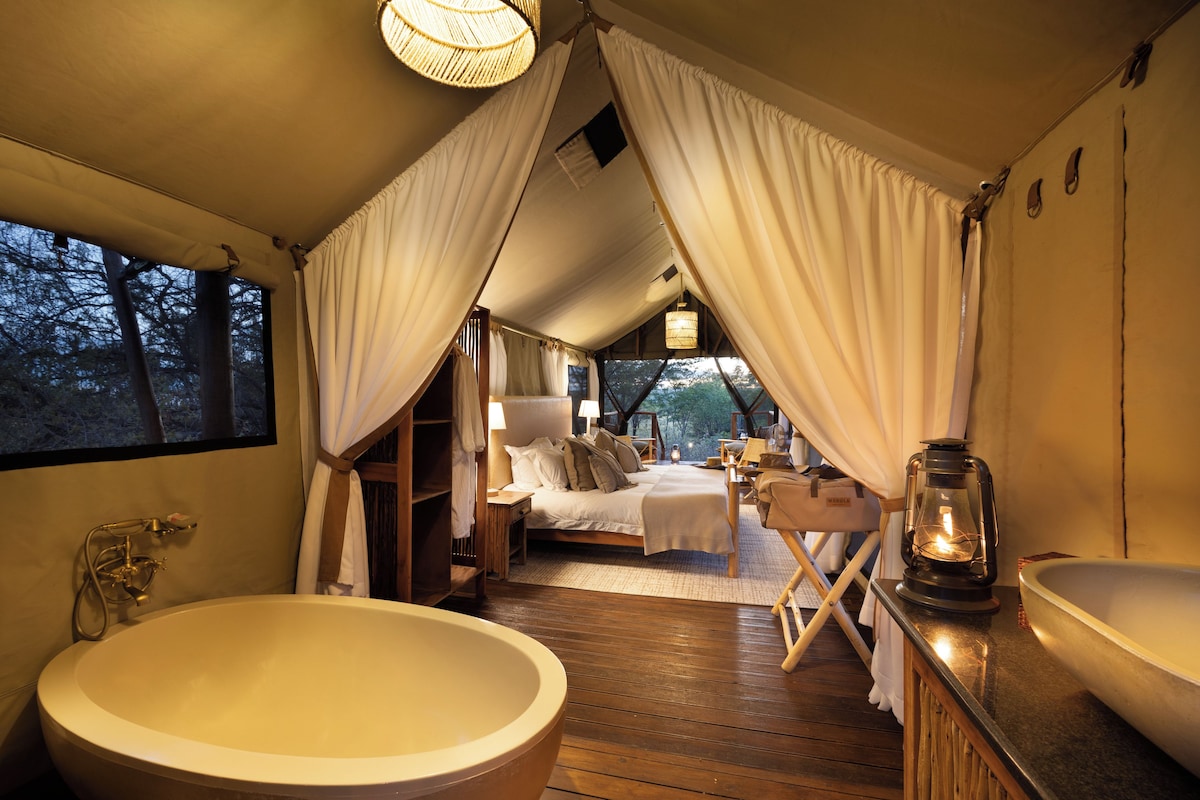 A cozy bedroom with a large bathtub, a wooden floor, and a view of the outdoors.
