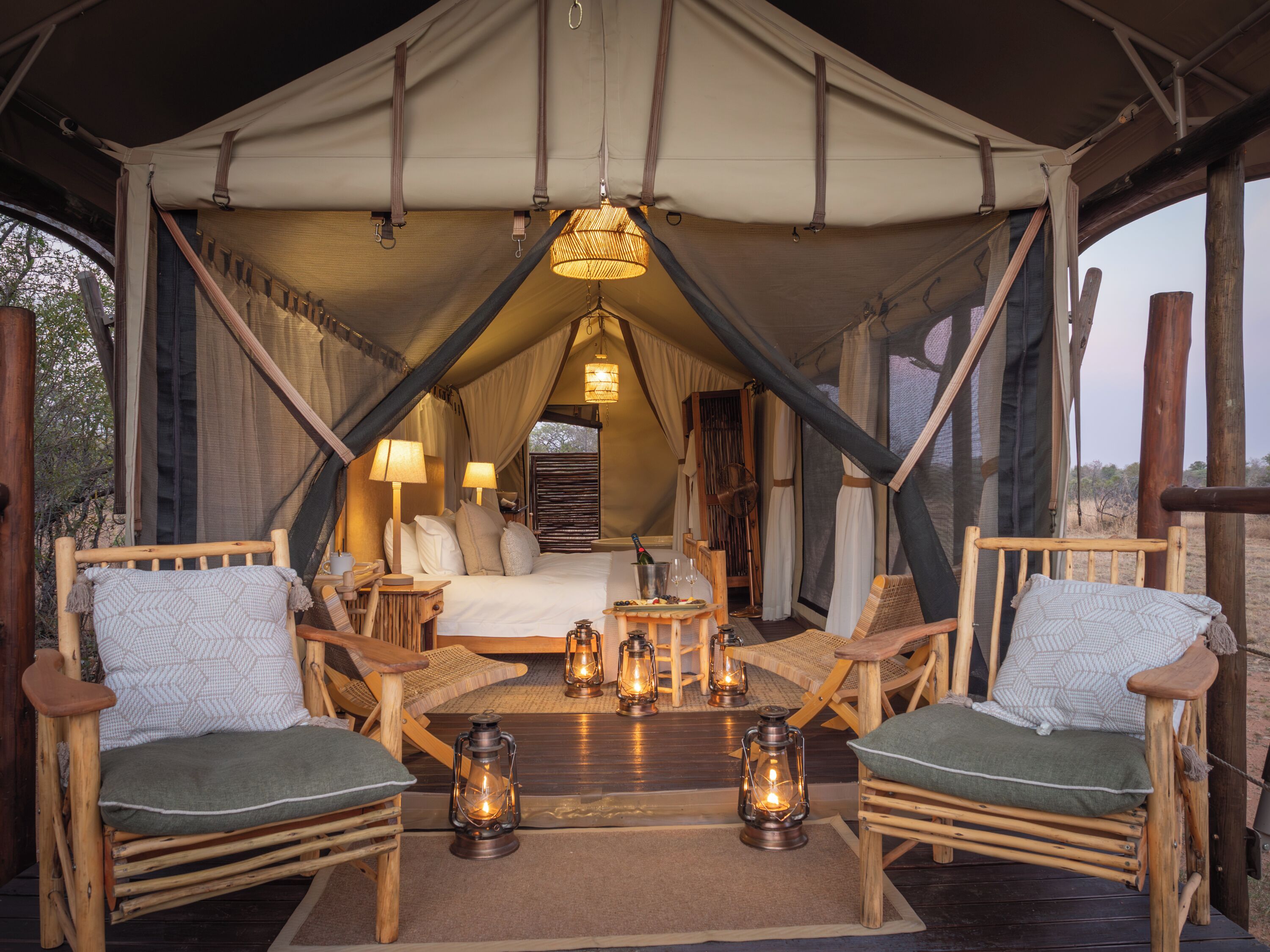 A tented accommodation with a bed, two wooden chairs, a small table, and multiple lanterns.