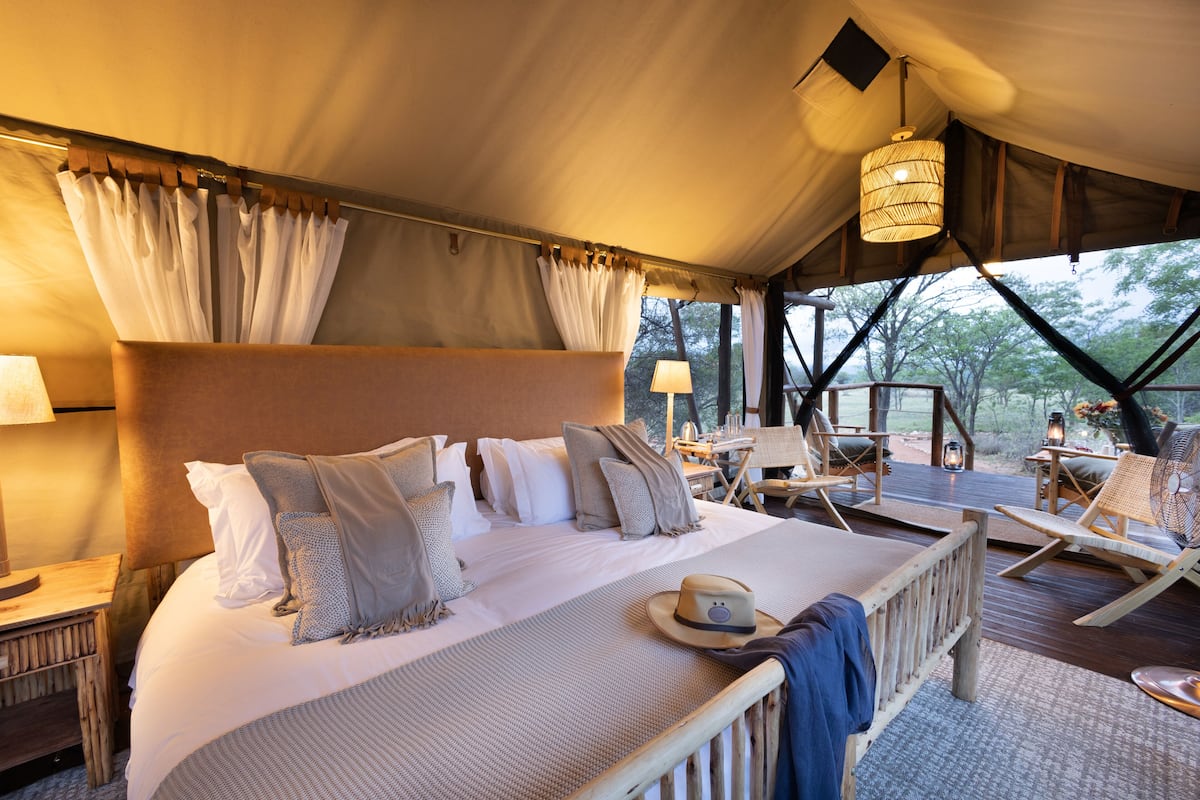 A spacious tented accommodation with a large bed, a dining area, and a view of the outdoors.
