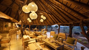 A cozy outdoor seating area with wicker furniture, a stone wall, and a thatched roof.