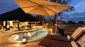 A pool area with lounge chairs, an umbrella, and a building with outdoor seating.