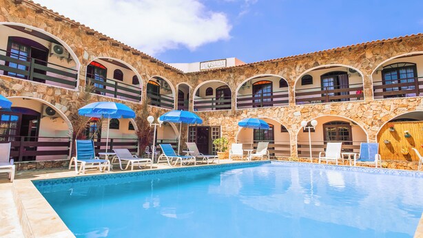 A courtyard with a swimming pool, lounge chairs, and umbrellas. - VELINN Pousada Casa de Pedra Ilhabela (Ilhabela)