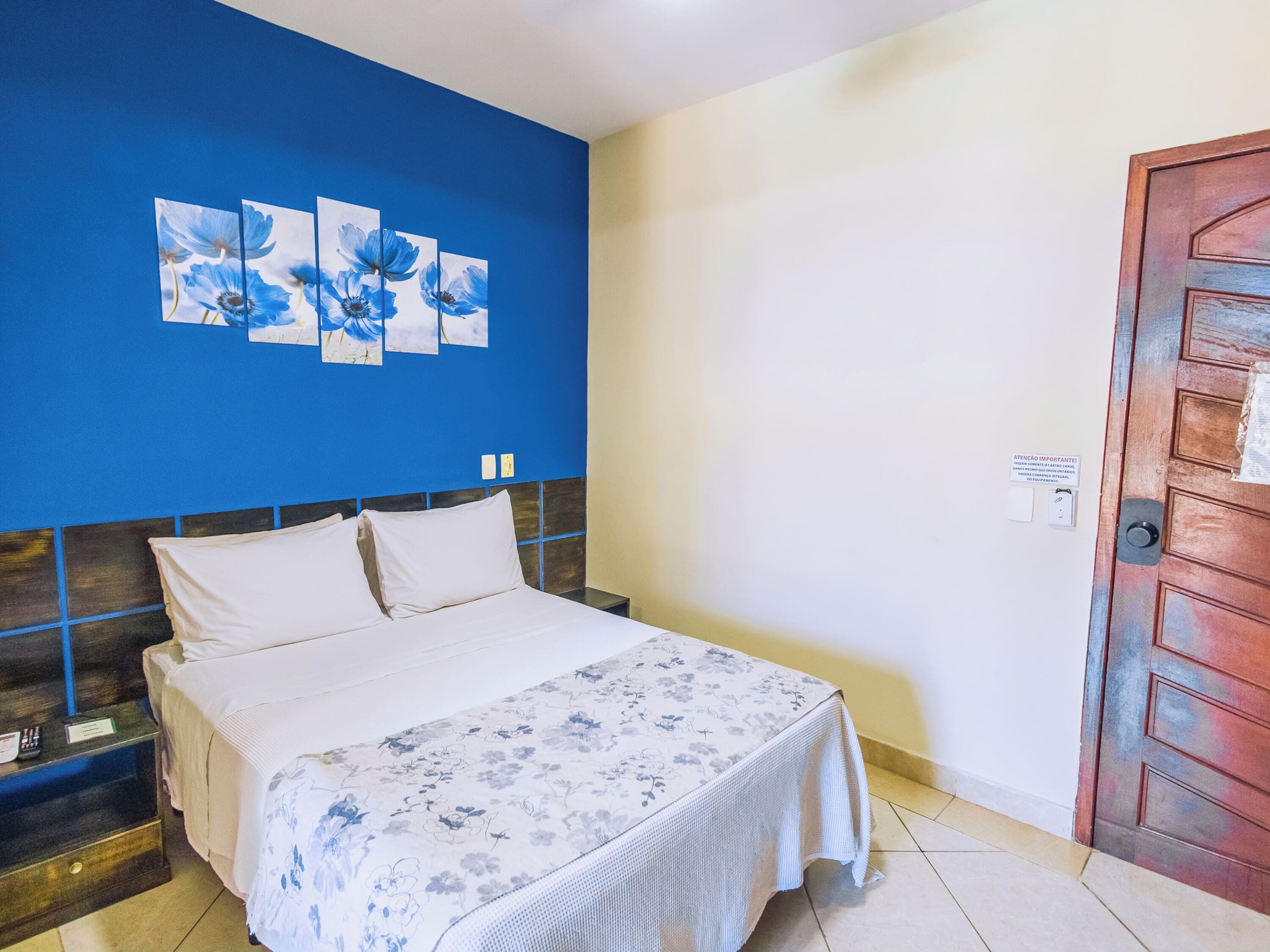 Habitación de hotel con cama, mesita de noche, pared azul con motivos florales y puerta de madera.
