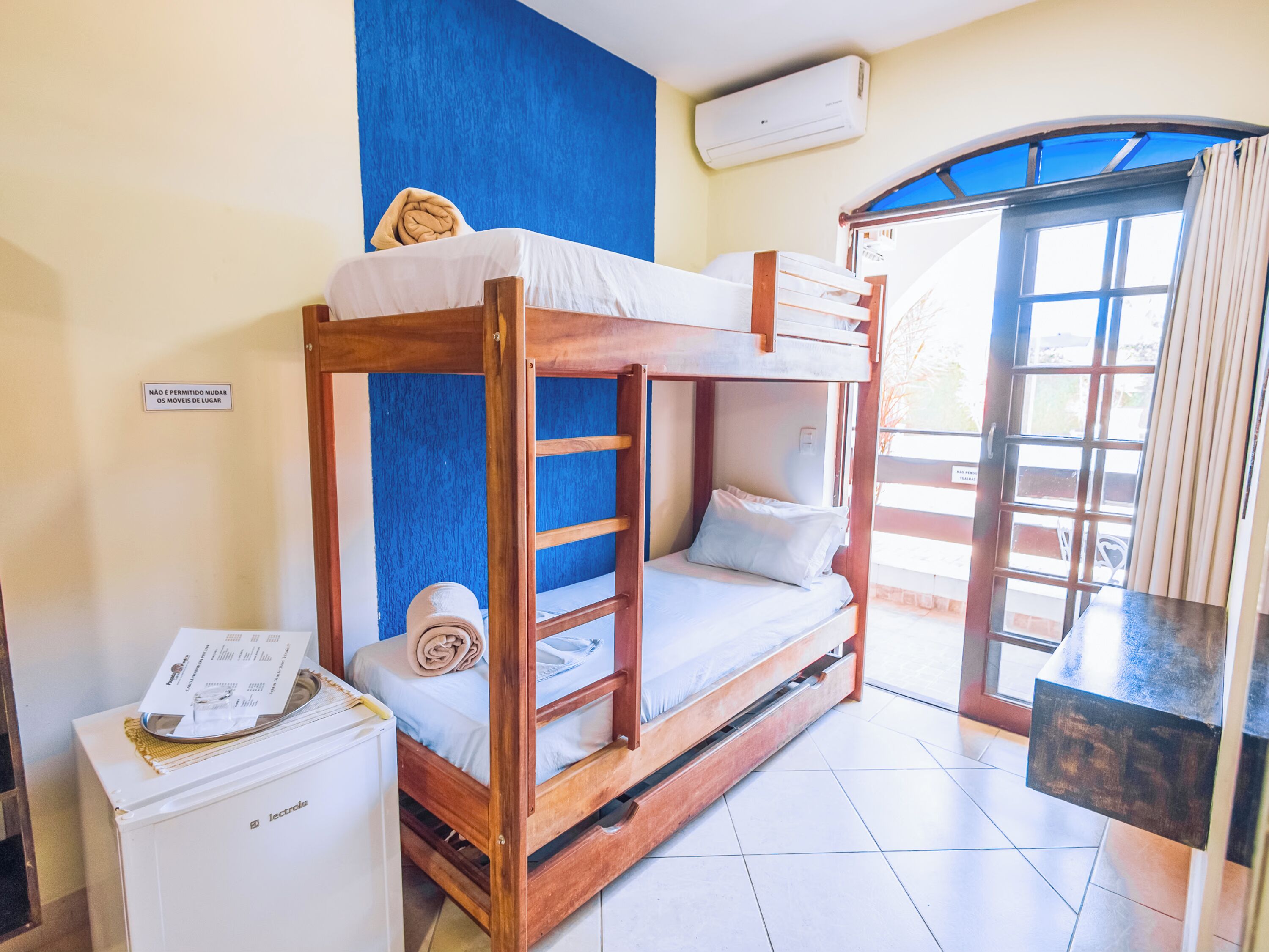 A bunk bed room with a blue wall, a window with curtains, and a refrigerator.