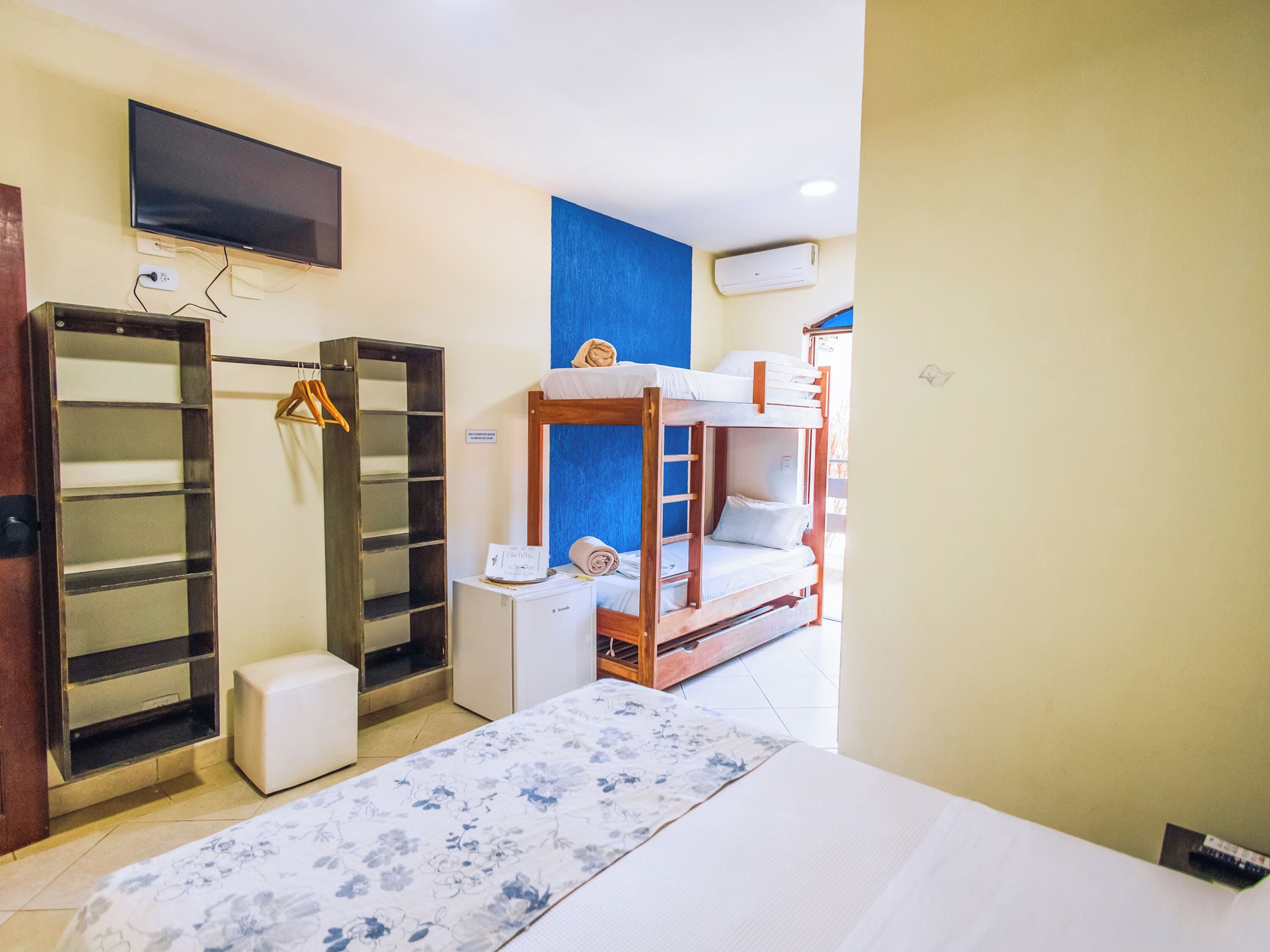 A room with bunk beds, a flat-screen TV mounted on the wall, a wardrobe, and a small desk with a chair.
