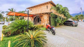 A stone building with a tiled roof, a covered parking area, and a parked motorcycle. - VELINN Pousada Casa de Pedra Ilhabela (Ilhabela)