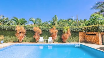 Piscina con sillones blancos y una pared de piedra.