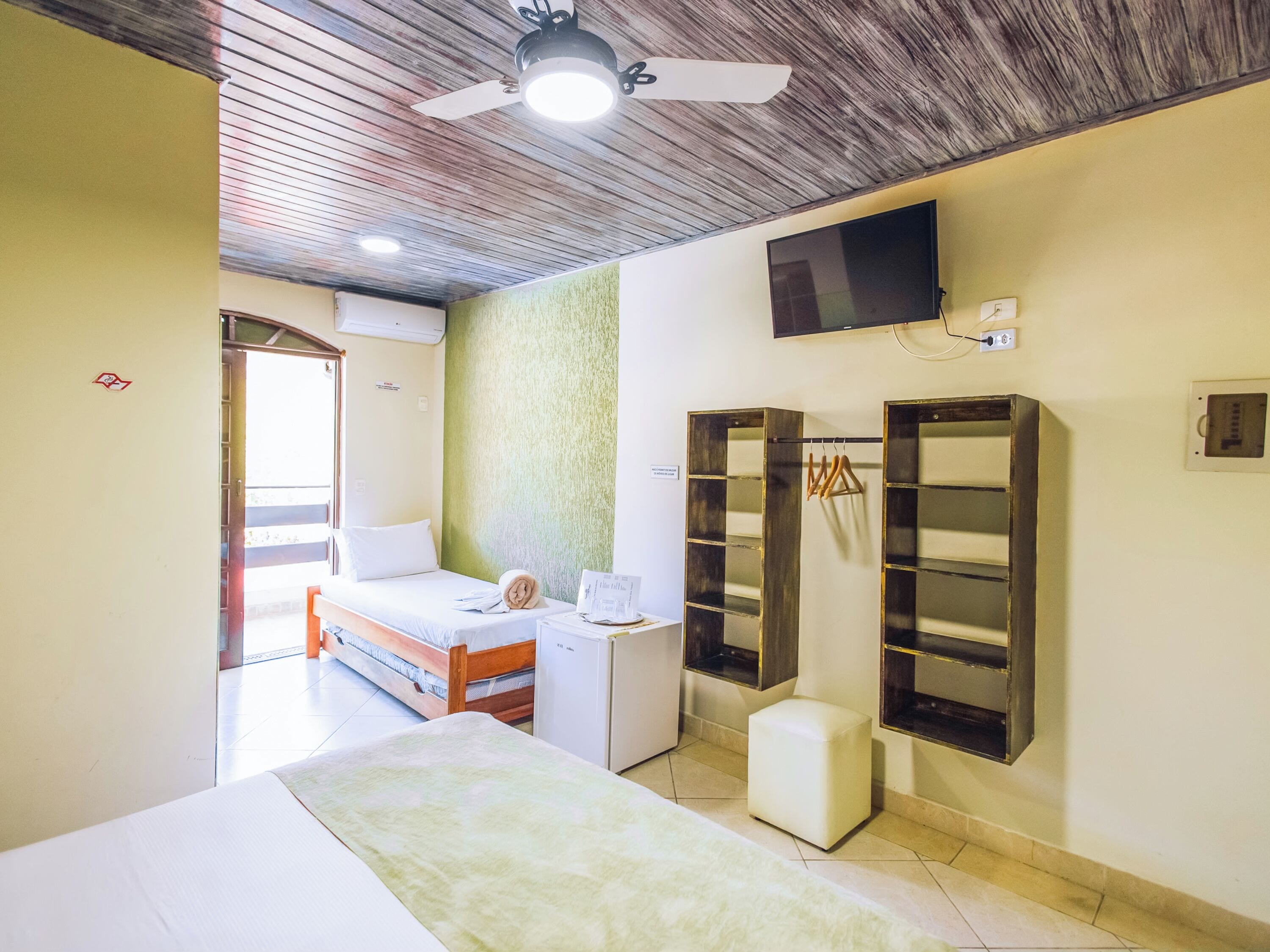 A hotel room with a bed, a small desk, a wardrobe, and a television mounted on the wall.