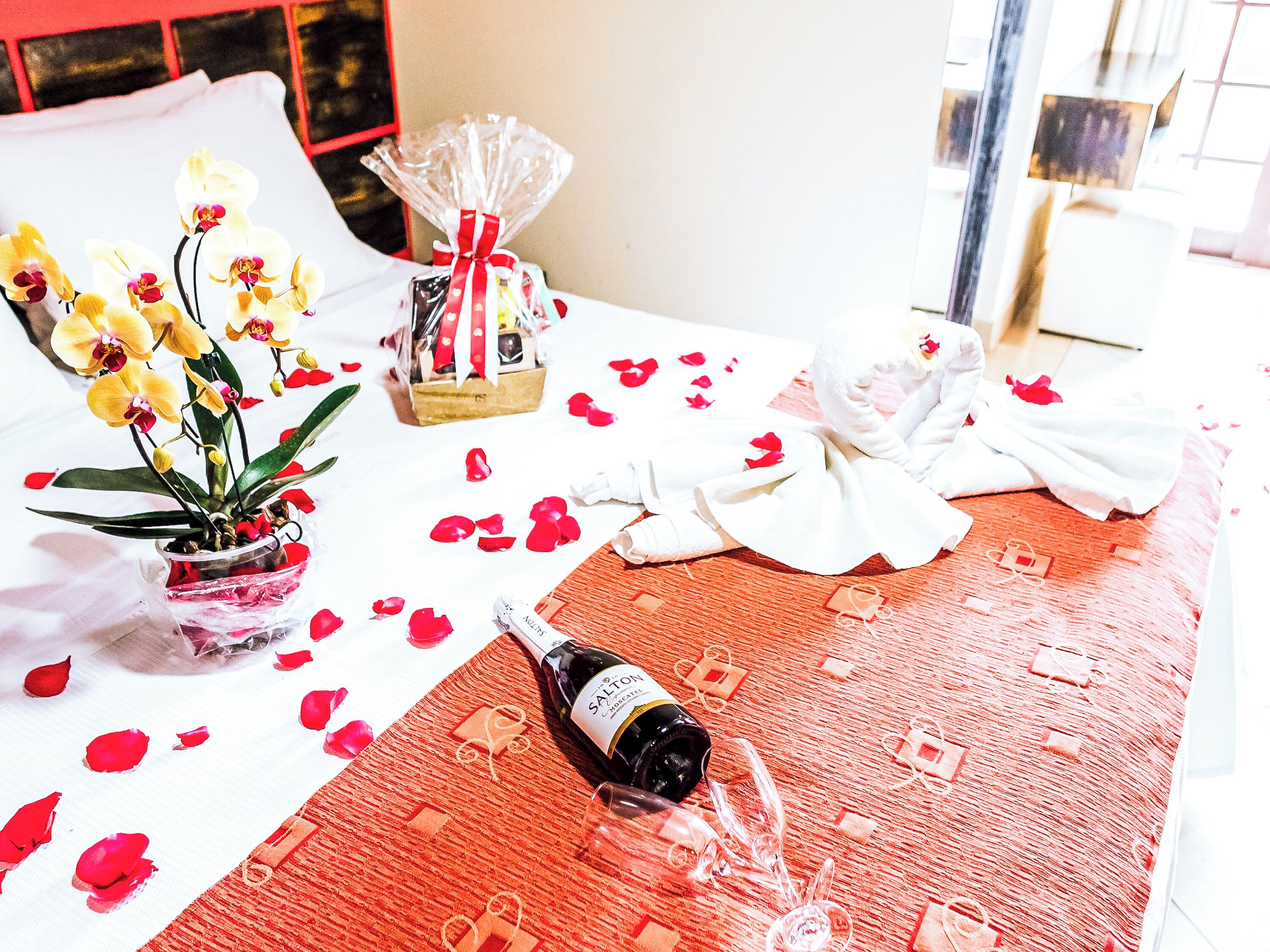 A bed with rose petals, a bottle of champagne, and a bouquet of orchids.