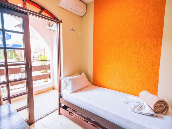 Una habitación pequeña con una cama individual y puerta corrediza de vidrio que da a un espacio exterior.