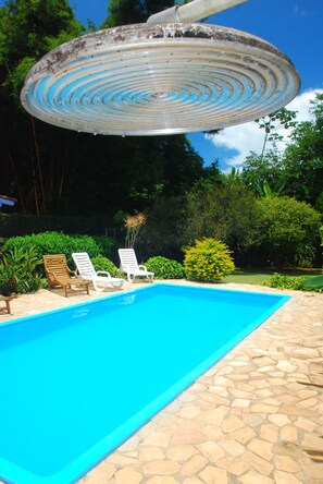 A swimming pool with a stone tiled edge, surrounded by lounge chairs and greenery. - Pousada do Sidão (Ilhabela)