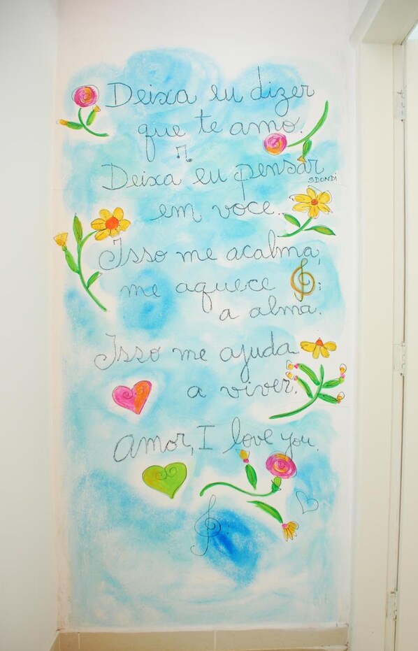 A wall with a watercolor painting of flowers and text expressing love. - Pousada do Sidão (Ilhabela)