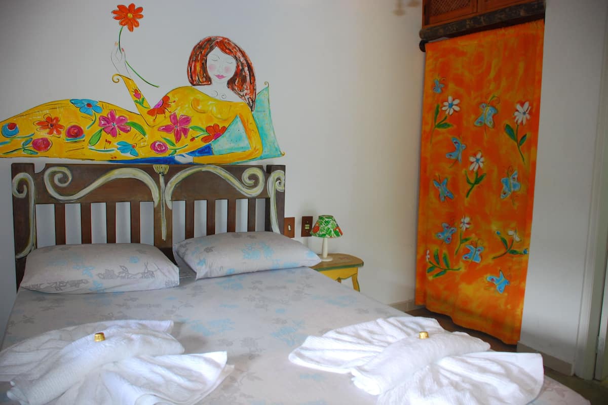 A bed with floral bedding, a headboard with a painting, and a wall tapestry.