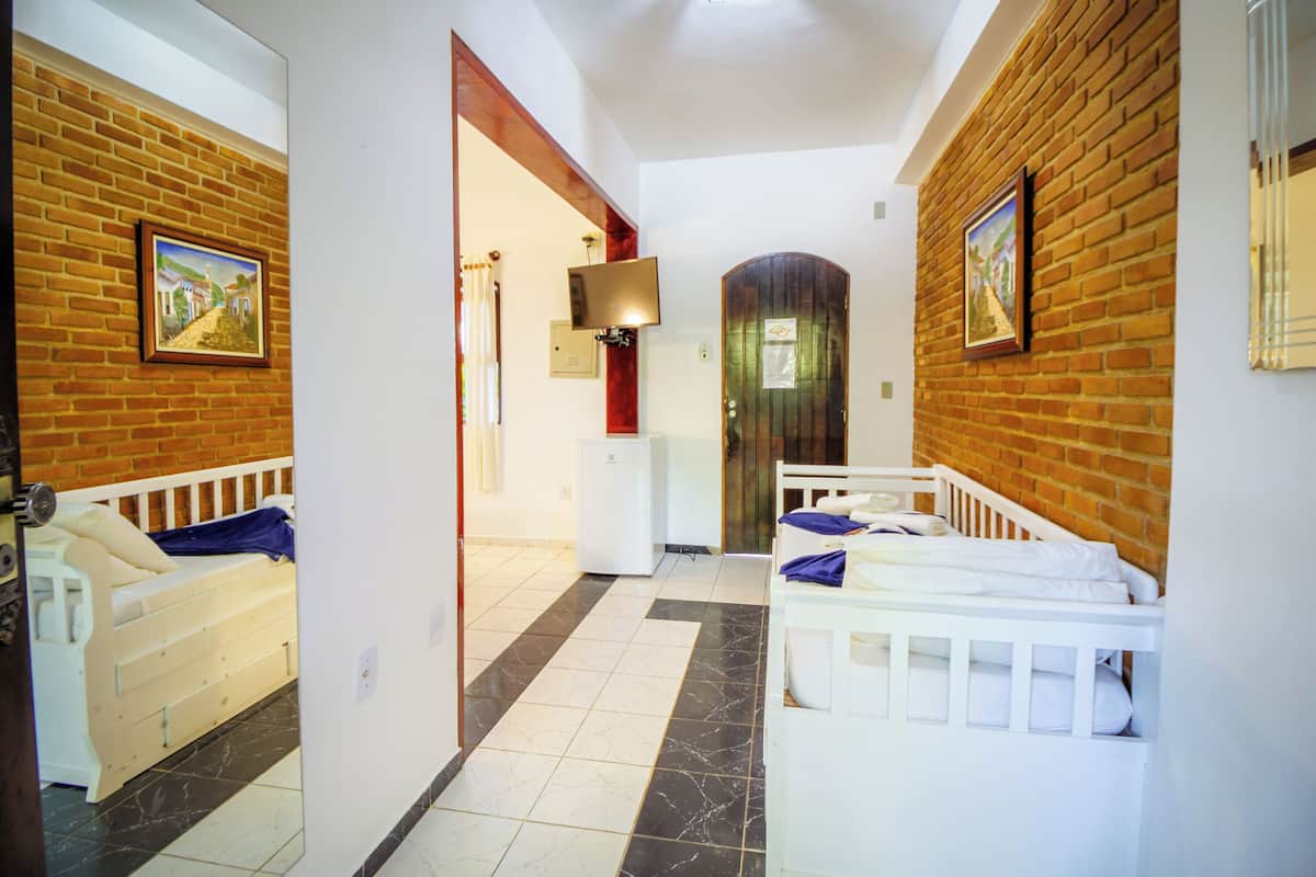 Une chambre d’hôtel avec un mur en briques, deux lits, une petite kitchenette et une porte donnant sur une autre pièce.