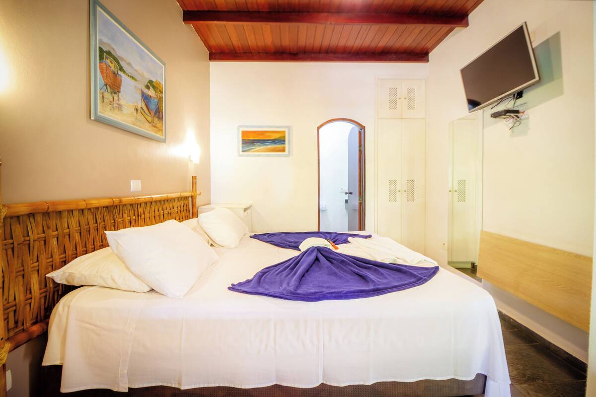 Une chambre d’hôtel avec un lit, une tête de lit en bois, un tableau au mur, un téléviseur fixé au mur et un miroir.