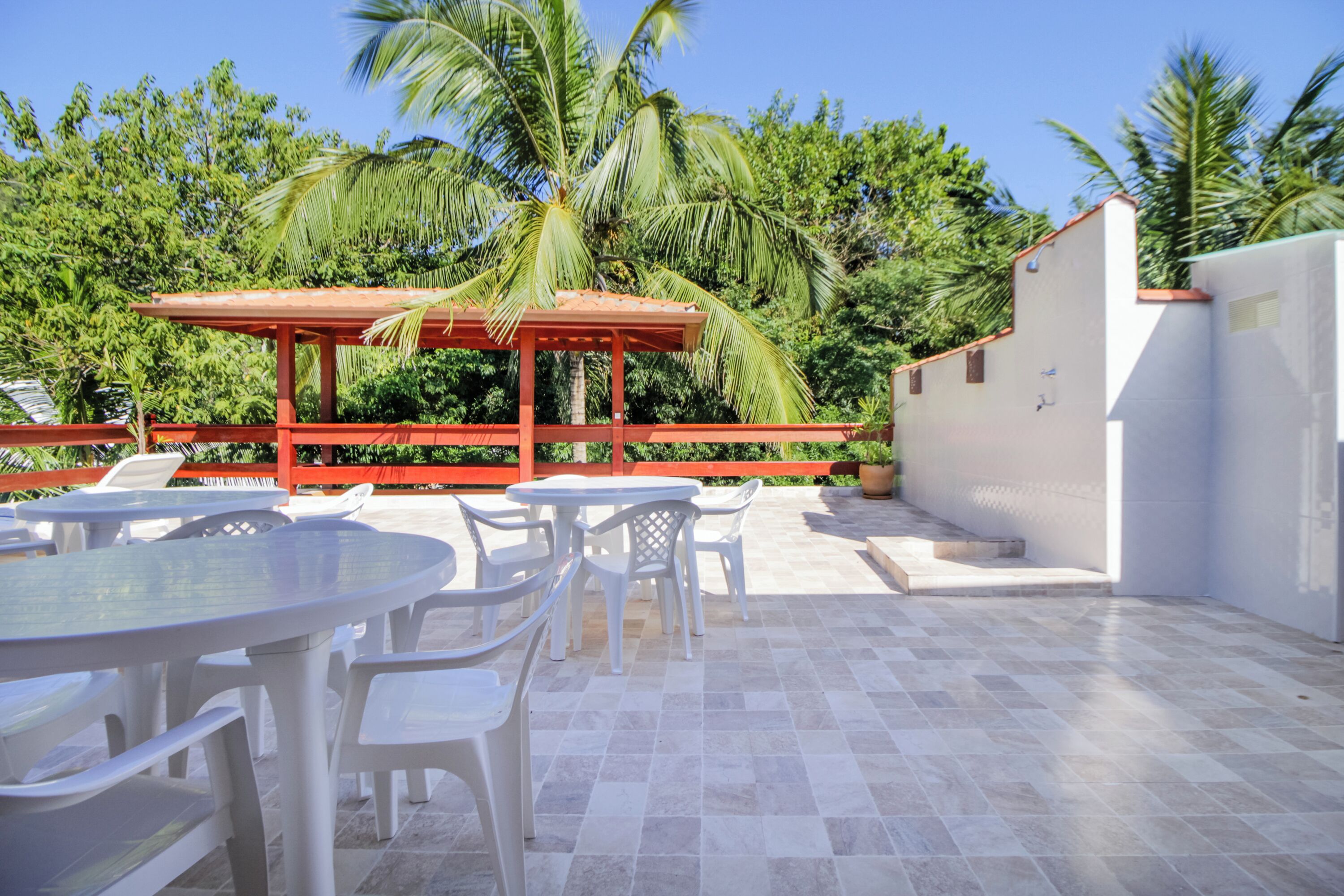 An outdoor patio area with round tables and chairs, a red pergola, and a white wall.