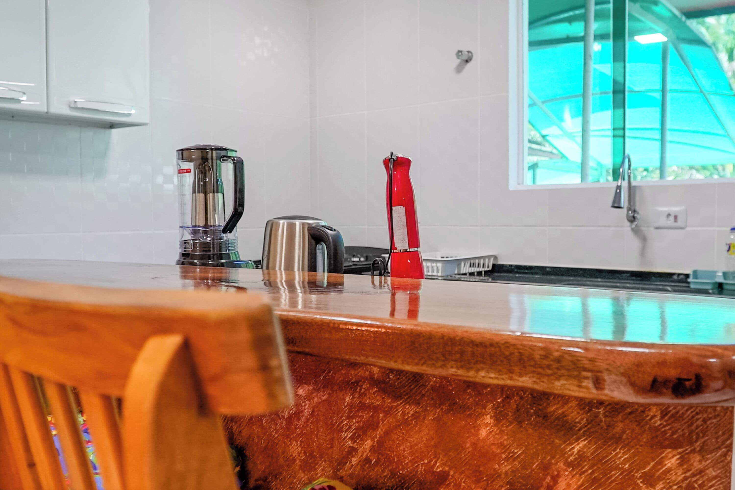 A kitchen with a wooden countertop, a kettle, a toaster, and a red bottle.