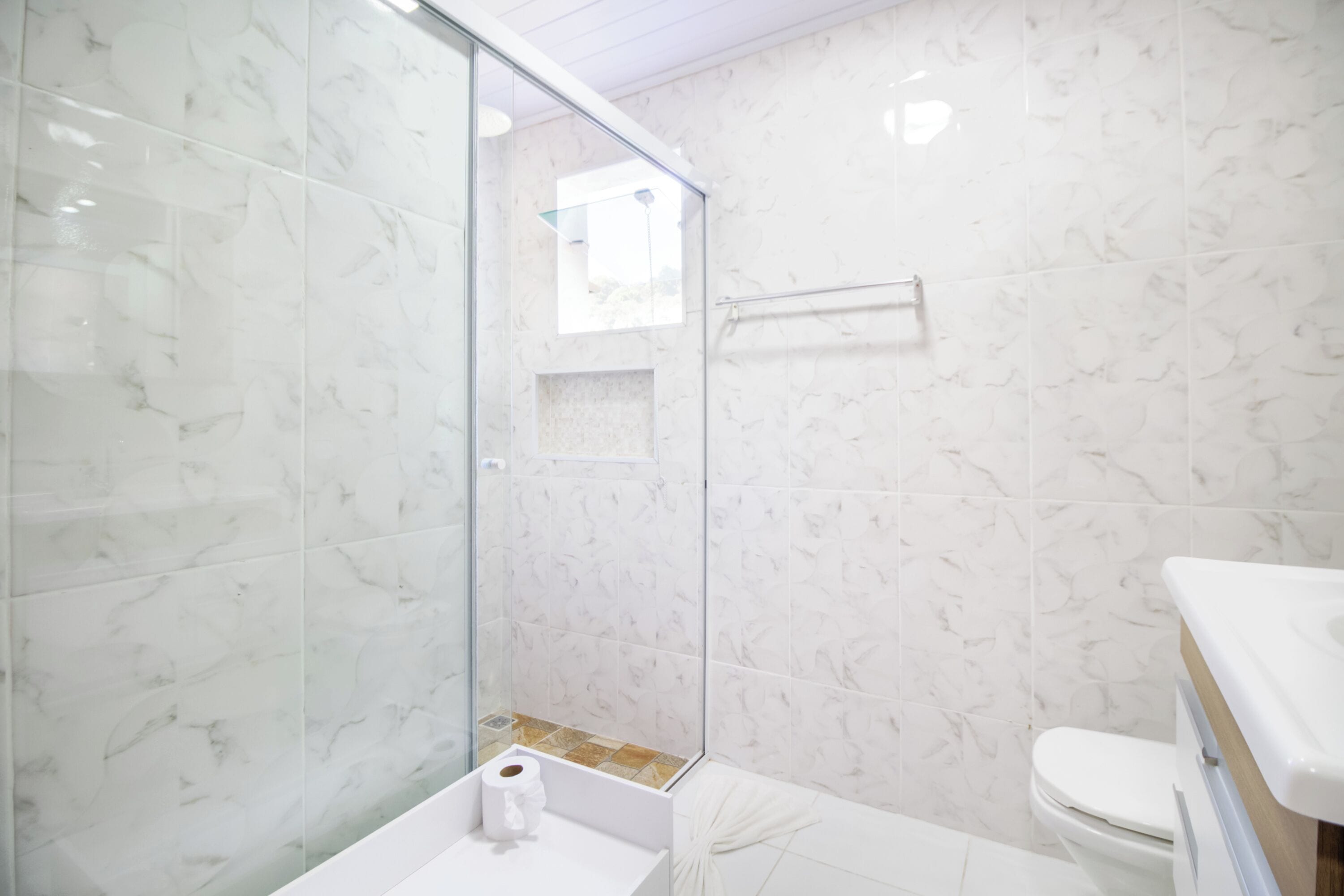 A bathroom with a glass shower enclosure, a white sink, and a toilet.