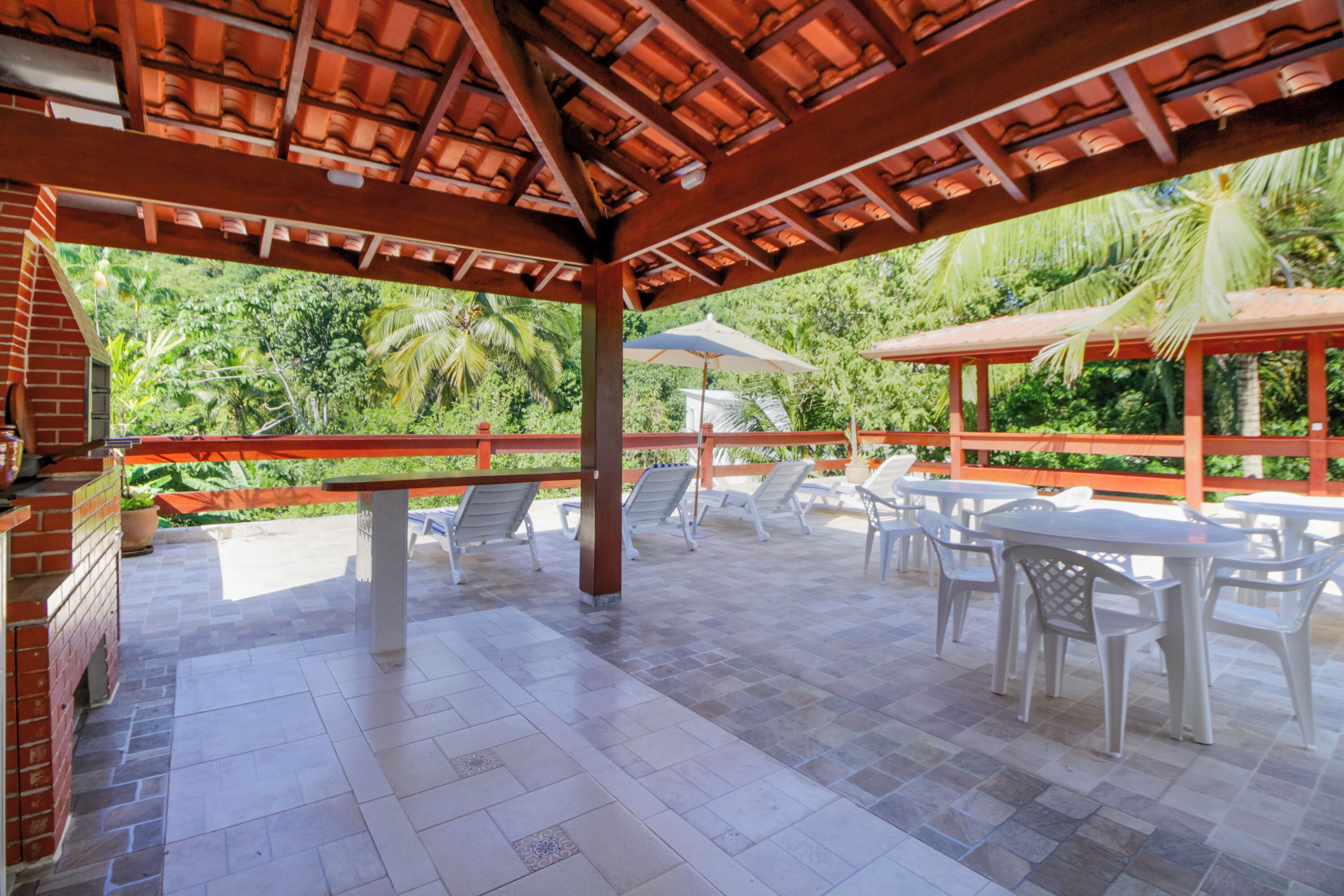 Um pátio externo com piso de azulejos, parede de tijolos e pérgola de madeira.