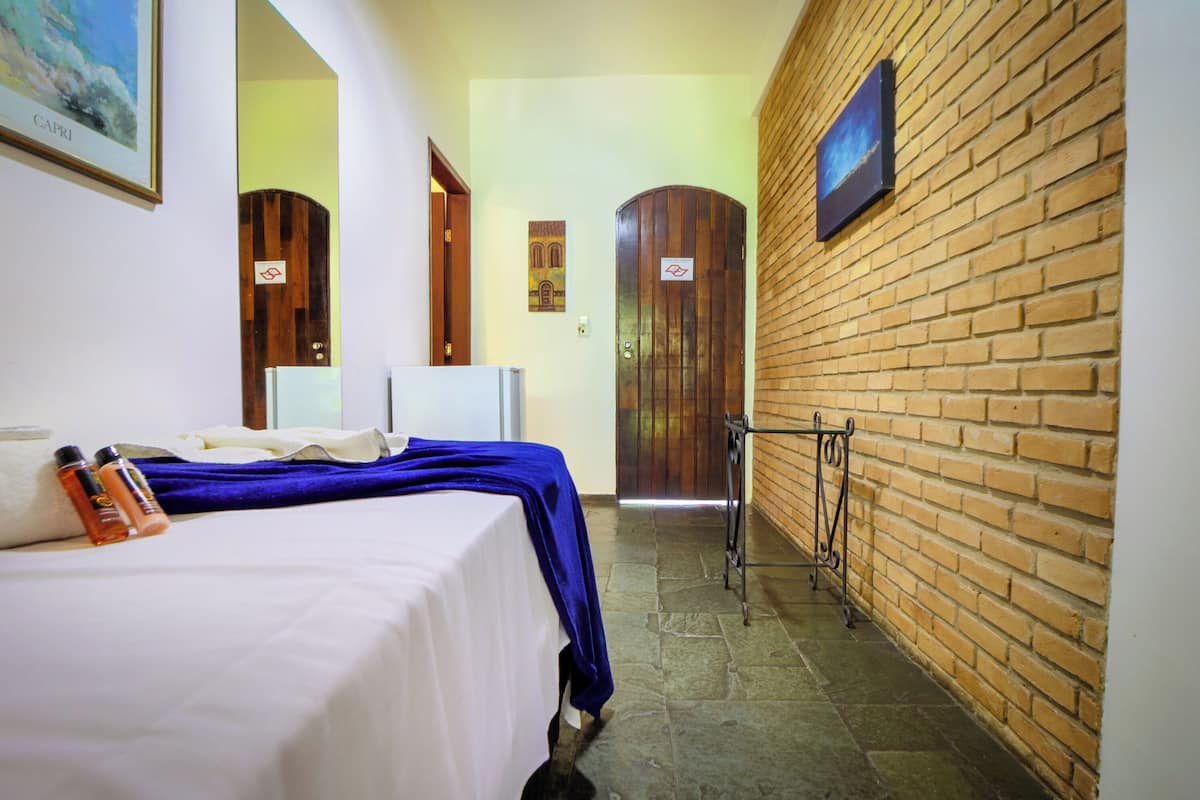 Une chambre d’hôtel avec un lit, une table de chevet, un miroir, un mur en briques et une porte.