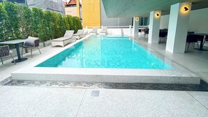 A modern indoor swimming pool with clear blue water, surrounded by lounge chairs and tables, and a covered area with seating. - The One Hotel Bay Breeze Pattaya (Pattaya)
