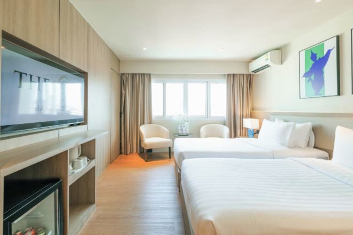 A hotel room with two beds, a TV, a minibar, and a large window with curtains.