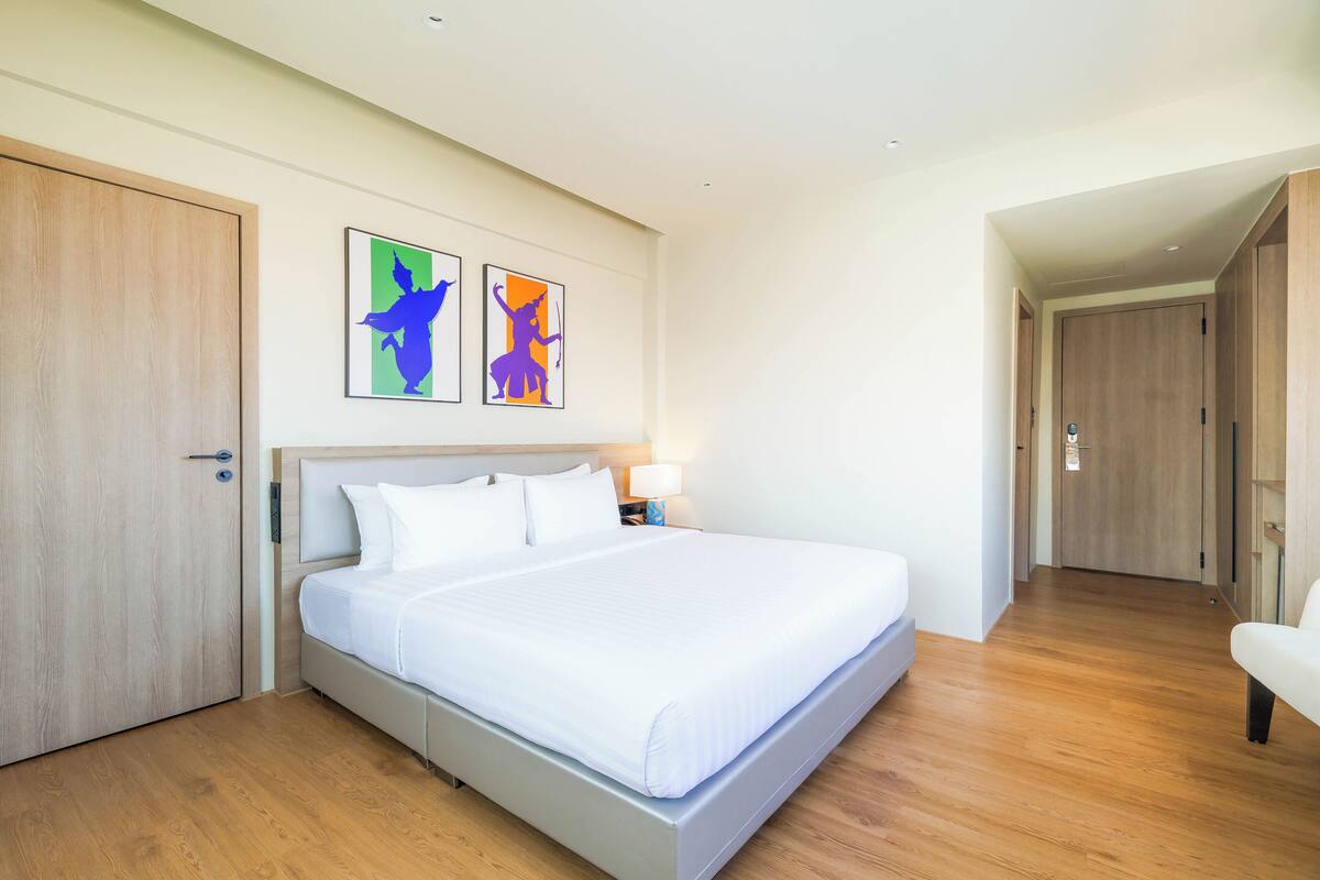 Une chambre d’hôtel avec un grand lit, un plancher en bois, une table de chevet avec une lampe et deux tableaux encadrés au mur.