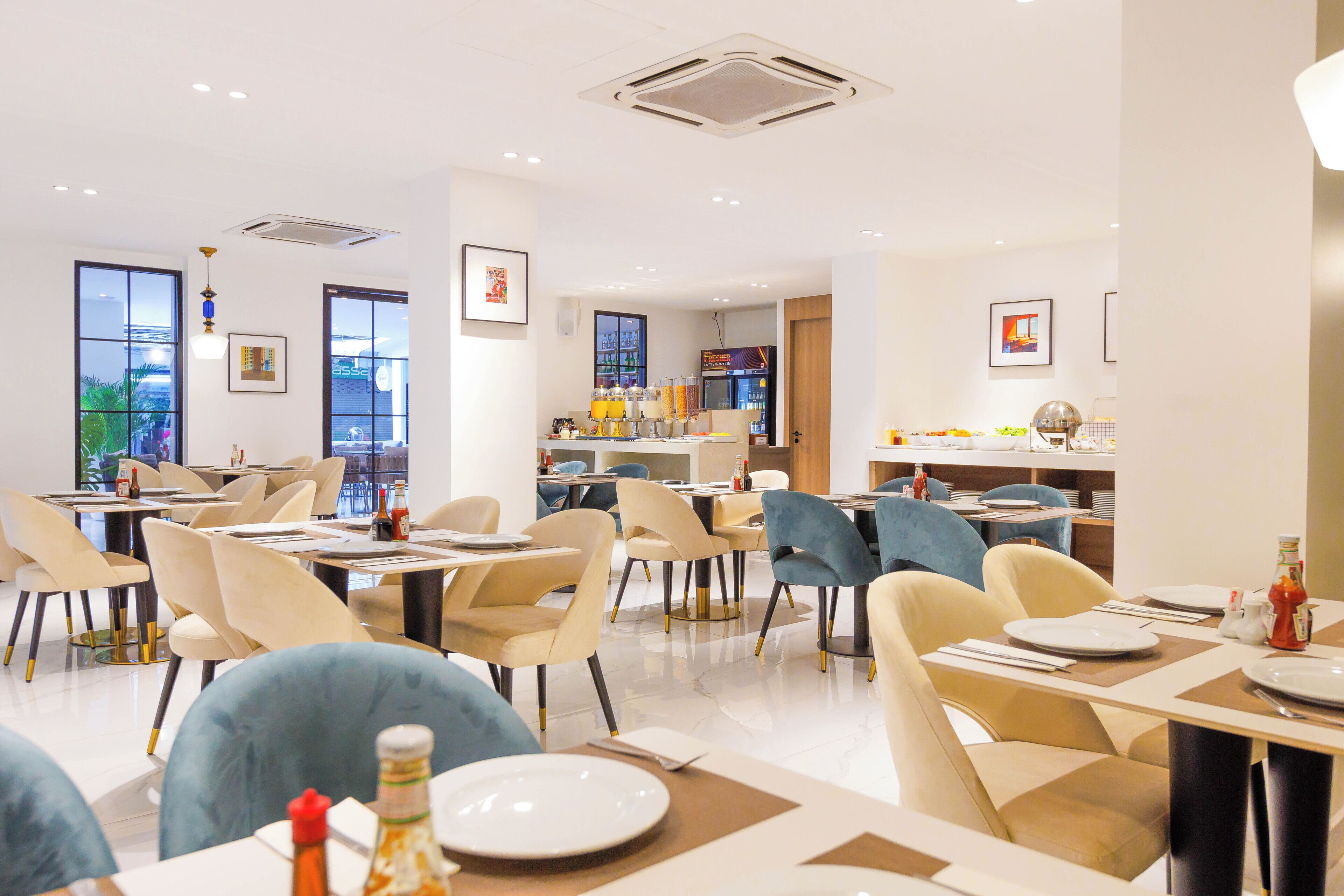 A modern dining area with tables and chairs, a refrigerator with beverages, and artwork on the walls.