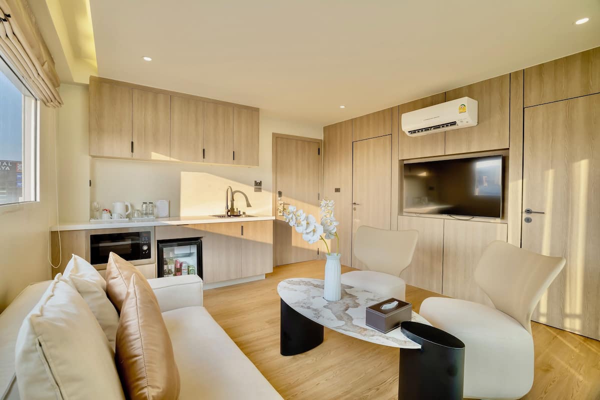Un salon moderne comprenant un canapé, une table basse et des fauteuils, un coin cuisine avec un four à micro-ondes, et un téléviseur fixé au mur.