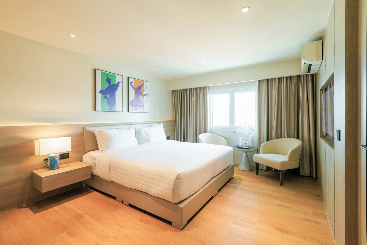 Une chambre d’hôtel avec un lit, une table de chevet, une lampe, une chaise et un tableau au mur.