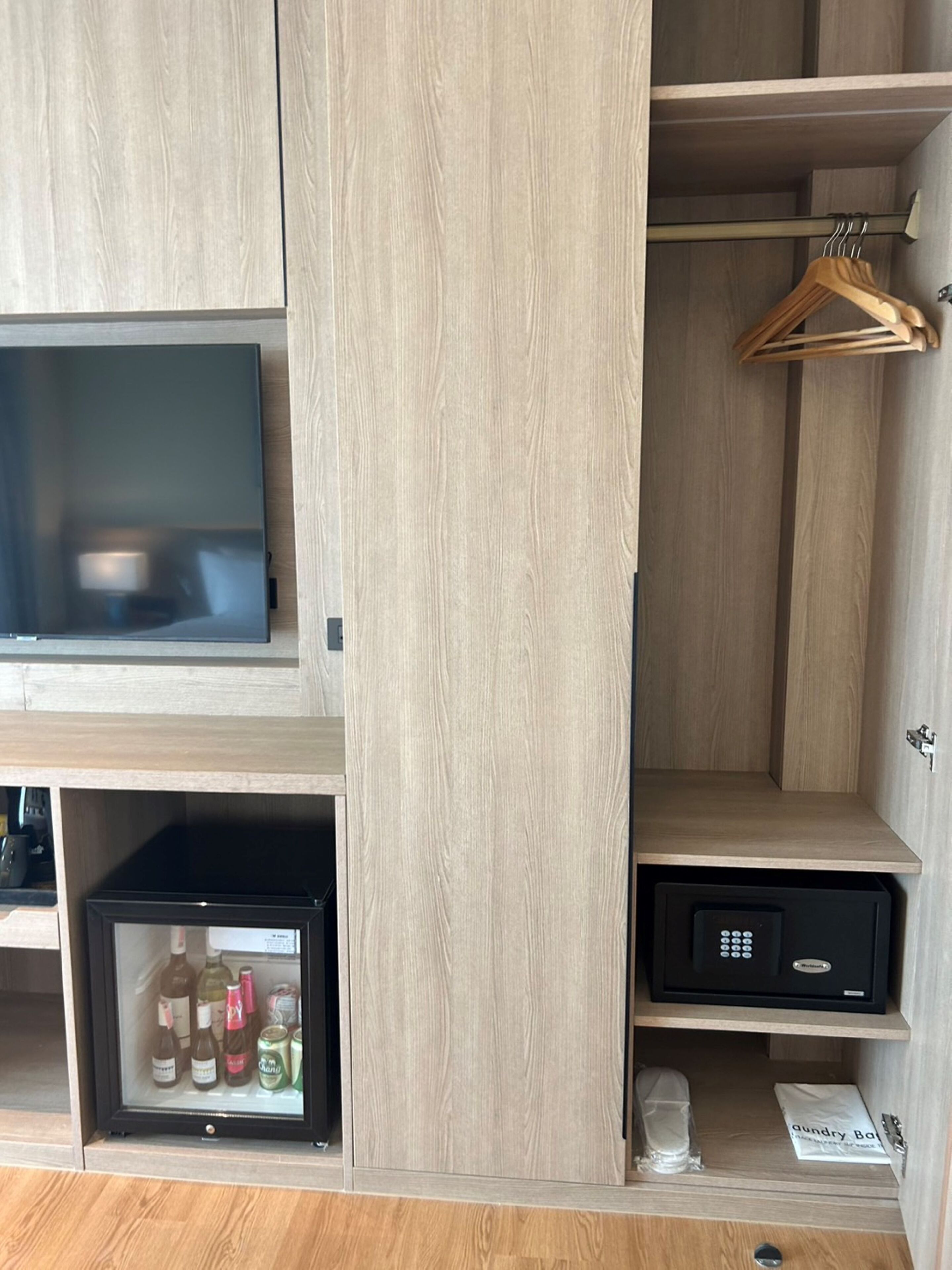 A hotel room with a wooden cabinet, a television, a minibar, and a safe.