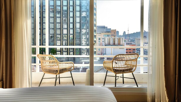 A hotel room with a large window, two wicker chairs, and a bed. - The One Hotel Bay Breeze Pattaya (Pattaya)