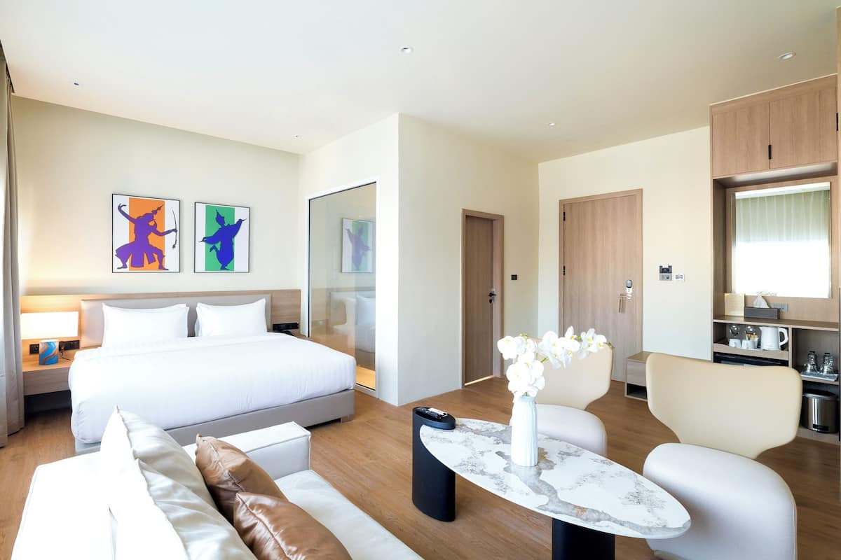 Une chambre d’hôtel moderne dotée d’un grand lit, d’un canapé, d’un coin repas avec une table et d’œuvres d’art accrochées aux murs.