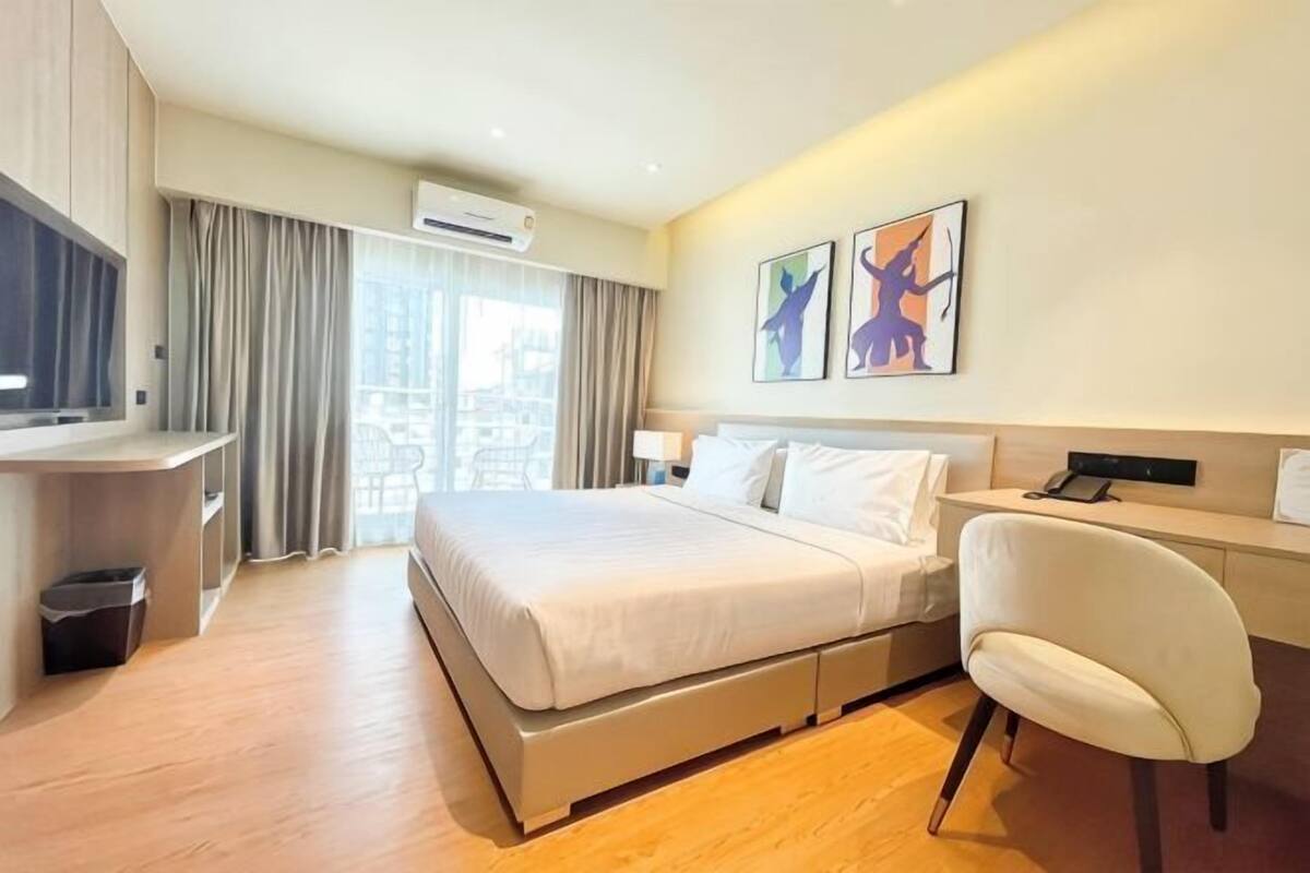 Une chambre d’hôtel équipée d’un lit, d’un bureau, d’une chaise, d’œuvres d’art et offrant une vue sur l’extérieur.