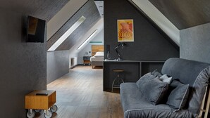 Un dormitorio en el ático con techo inclinado, un sofá gris, un escritorio y un cuadro.
