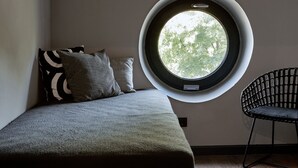 Un dormitorio con un tragaluz circular, una cama, dos almohadas y una silla.