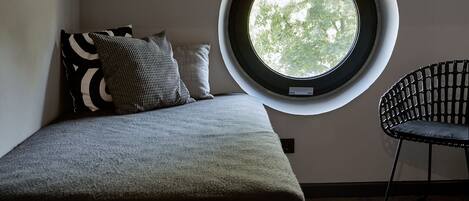 Quarto com um claraboia circular, uma cama, duas almofadas e uma cadeira.